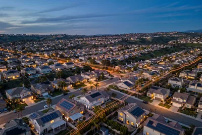 Vue aérienne d’un quartier résidentiel californien au crépuscule, maisons équipées de panneaux solaires et lignes électriques éclairées